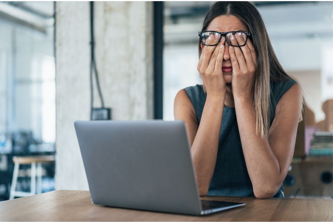 Woman in a modern office sitting in front of her laptop with her head in her hands and glasses on her head