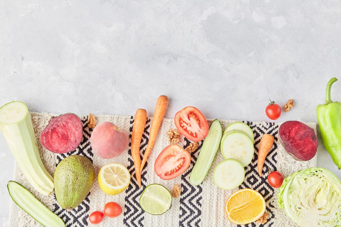colourful display of vegetables on a black and white blanket, with tomatoes, carrots, courgettes, oranges, peppers, and radishes