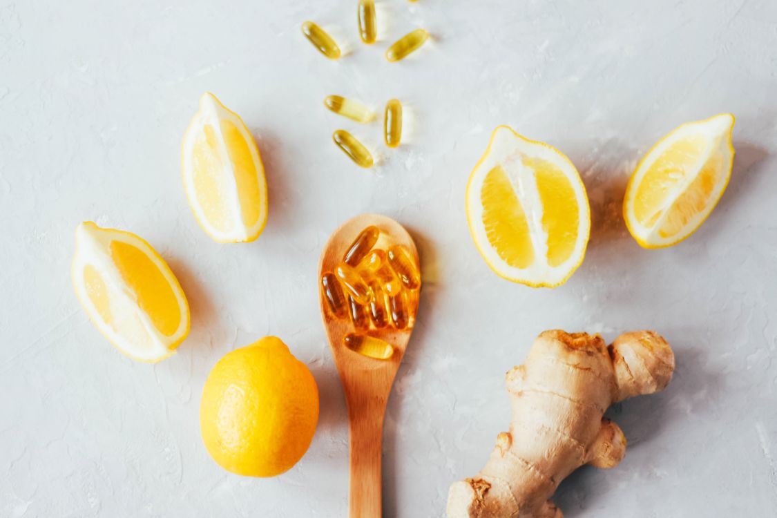 lemons, ginger root, spoon with supplements on, fish oil supplements, grey background