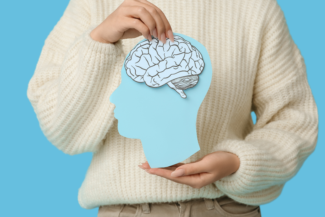 woman holding a graphic head with a brain and a cream jumper with a blue background