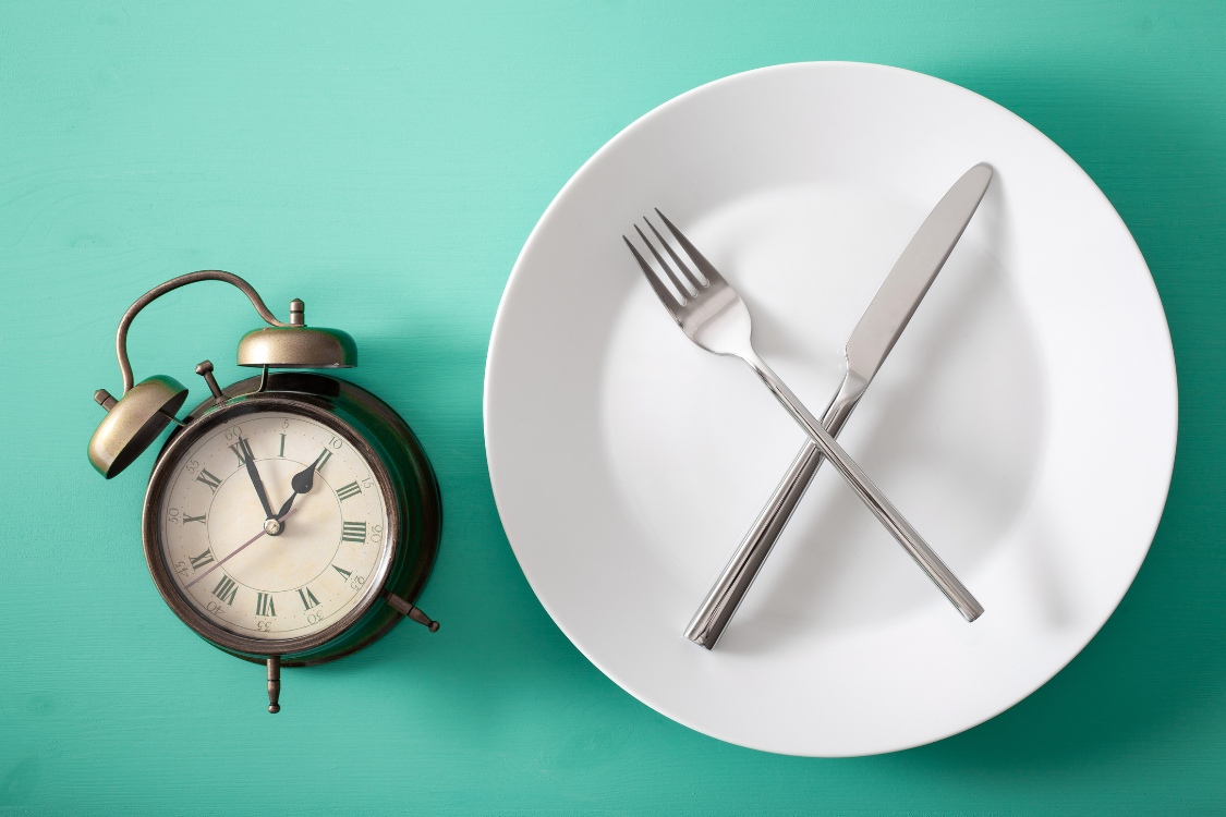 alarm clock and white plate with cutlery and a teal background