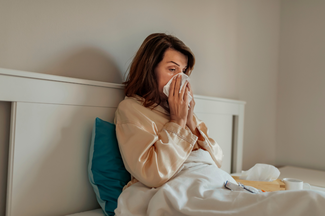woman sneezing in bed with a blue pillow and white bed sheets