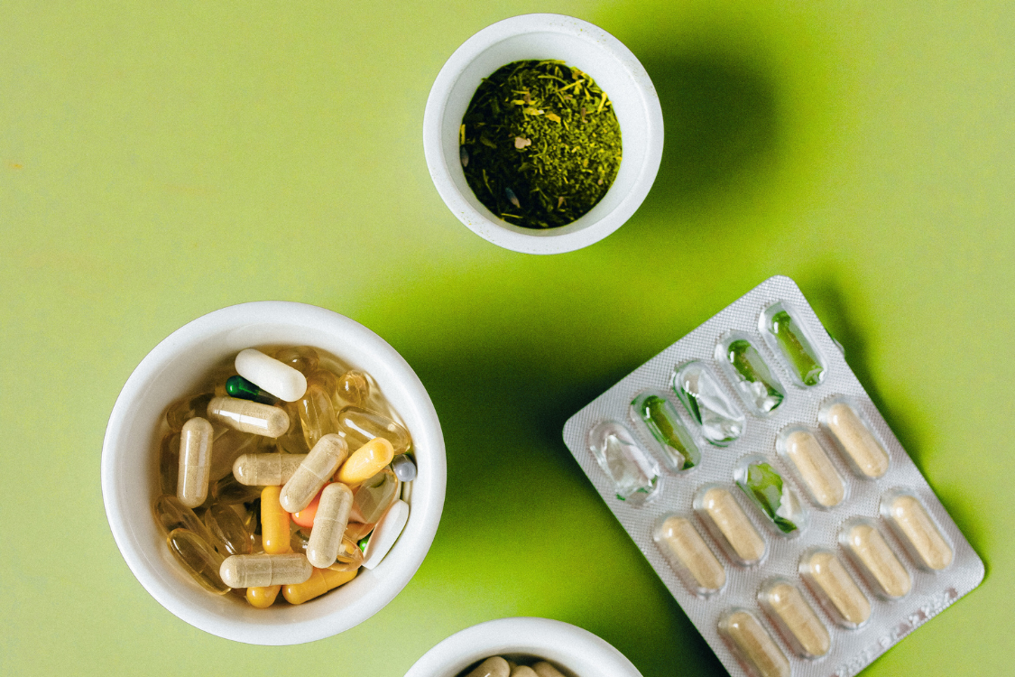 supplements and tablets and a bowl of green herbs with a green background, nutrients, phytonutrients, vitamins, supplements
