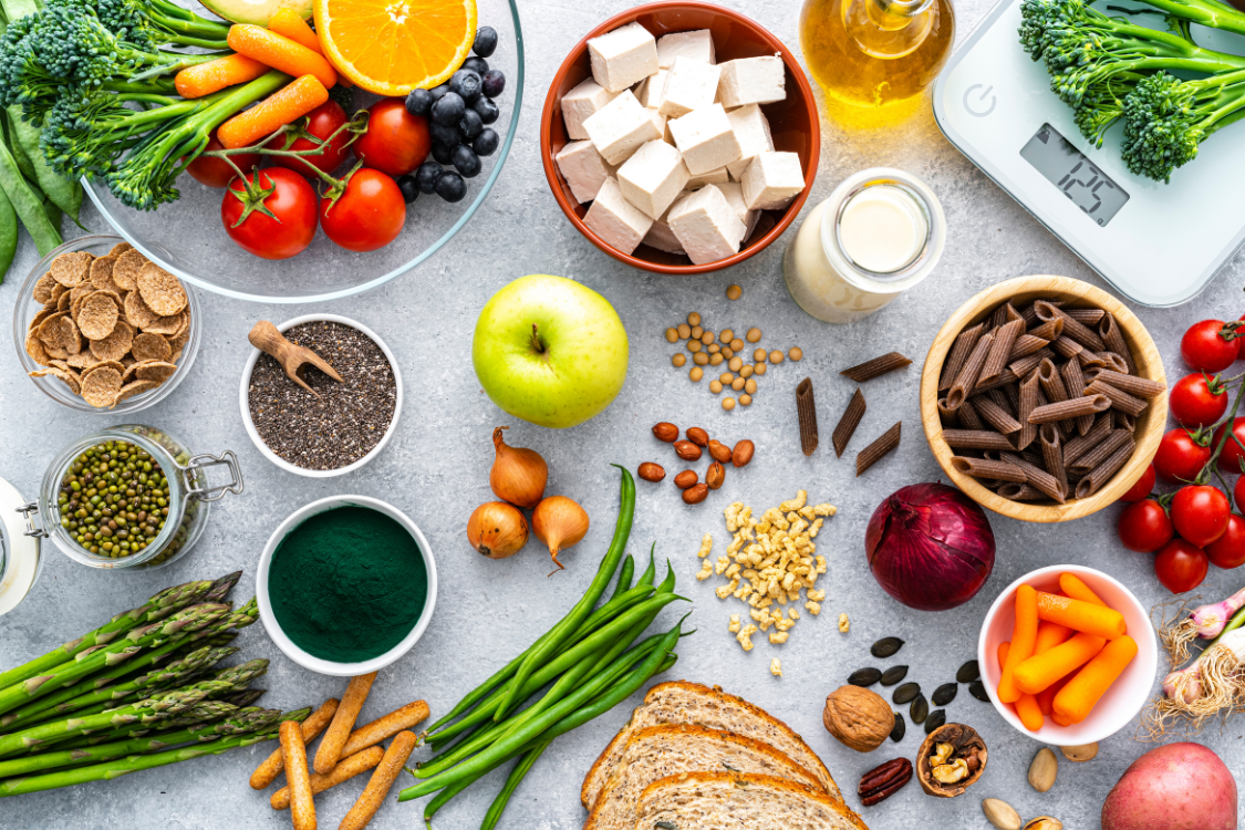different types of colourful plant based foods with a weighing scale on a grey background