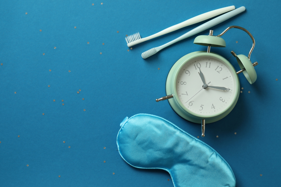 sleeping eye mask, clock, and toothbrushes on a blue background