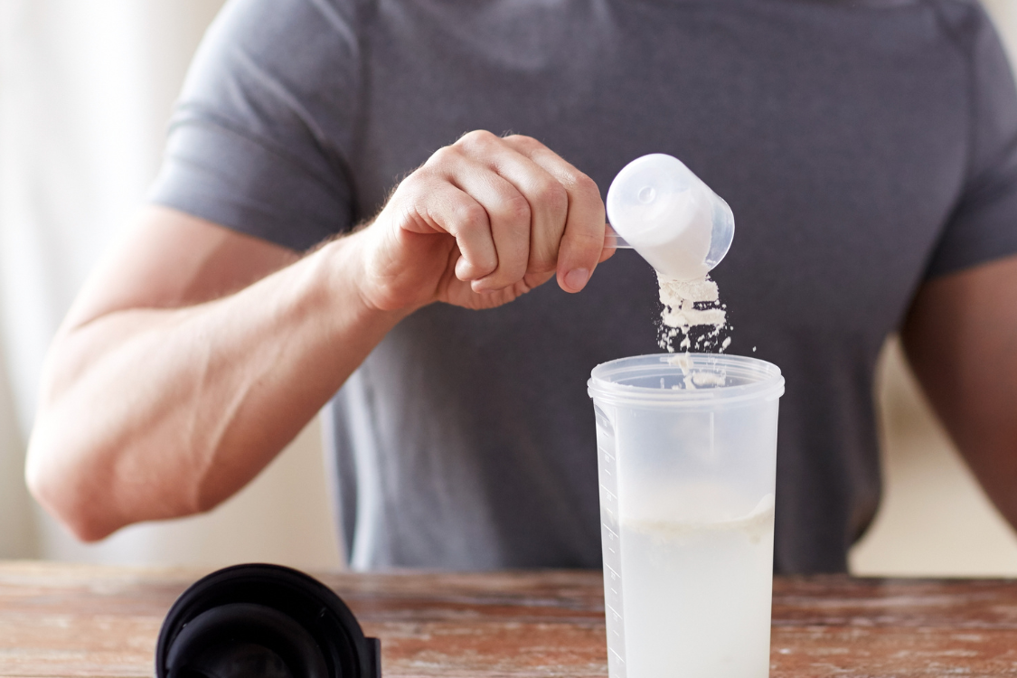 man with grey t-shirt pouring creatine into a plastic drinking cup