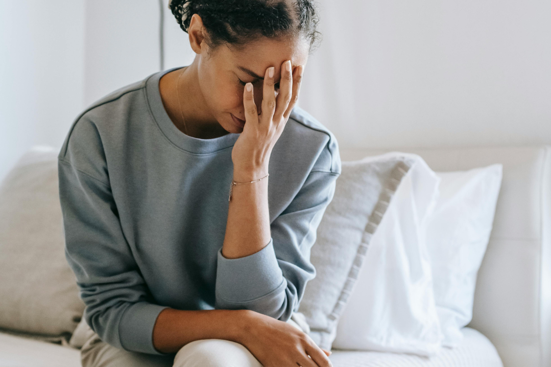 woman with head in hands with fatigue on white sofa