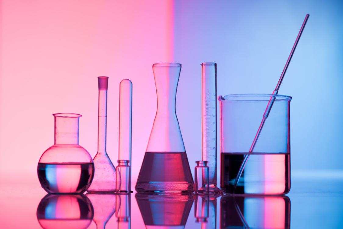 laboratory equipment including vials, conical flasks, test tubes, and a mixing pot filled with liquid set against a modern pink and blue background